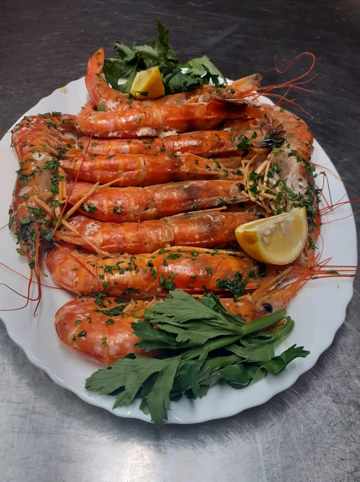 Un piatto di gamberoni conditi con prezzemolo, con uno spicchio di limone.